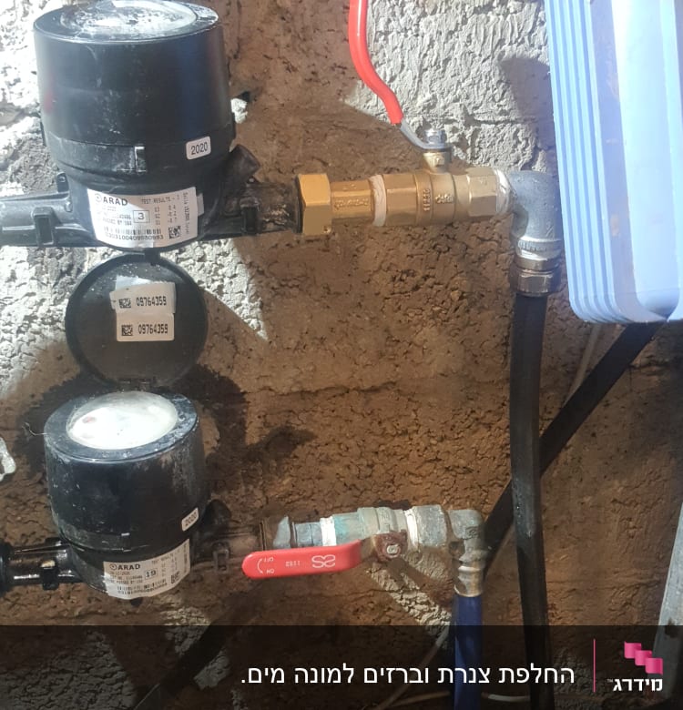 מד מים, ברזים וצינורות על קיר בטון